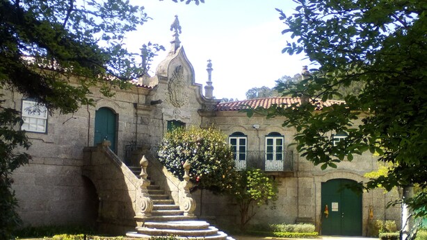 Un edificio de piedra con una escalera que conduce a una puerta verde, rodeado de jardines cuidados y árboles.