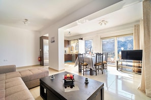 A spacious living area with a sofa, a coffee table with candles, a TV, and a balcony with a view.