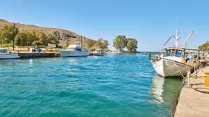 A marina with several boats docked, a clear sky, and a hilly landscape in the background. - Lake View Suites (Apokoronas)