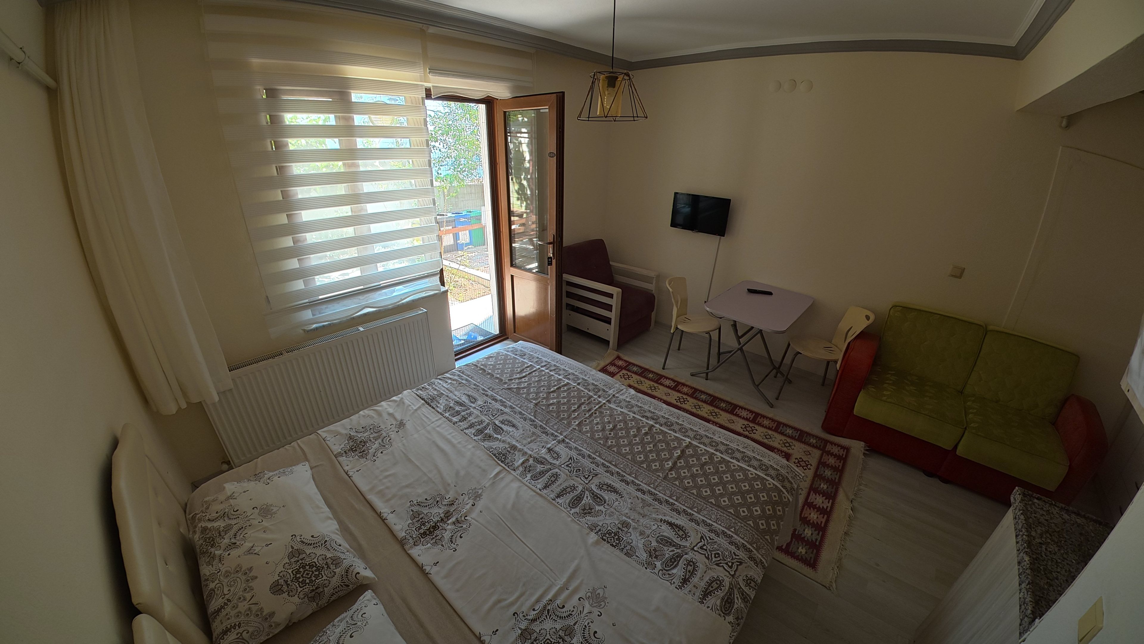 A bedroom with a bed, a desk, a chair, a television, and a sofa.