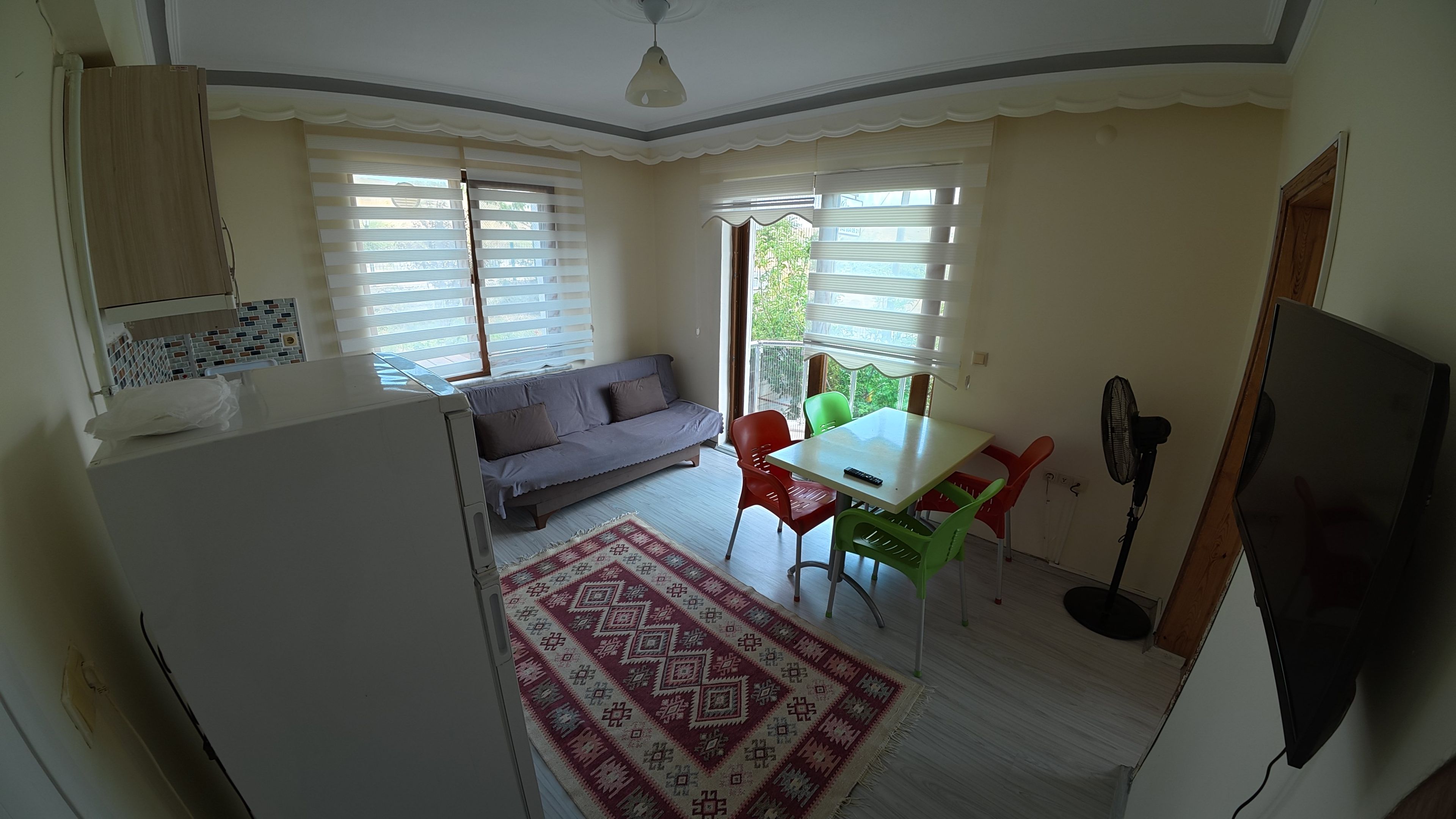 Un espacio habitable compacto con kitchenette, un sofá, una mesa de comedor con sillas y una alfombra estampada.