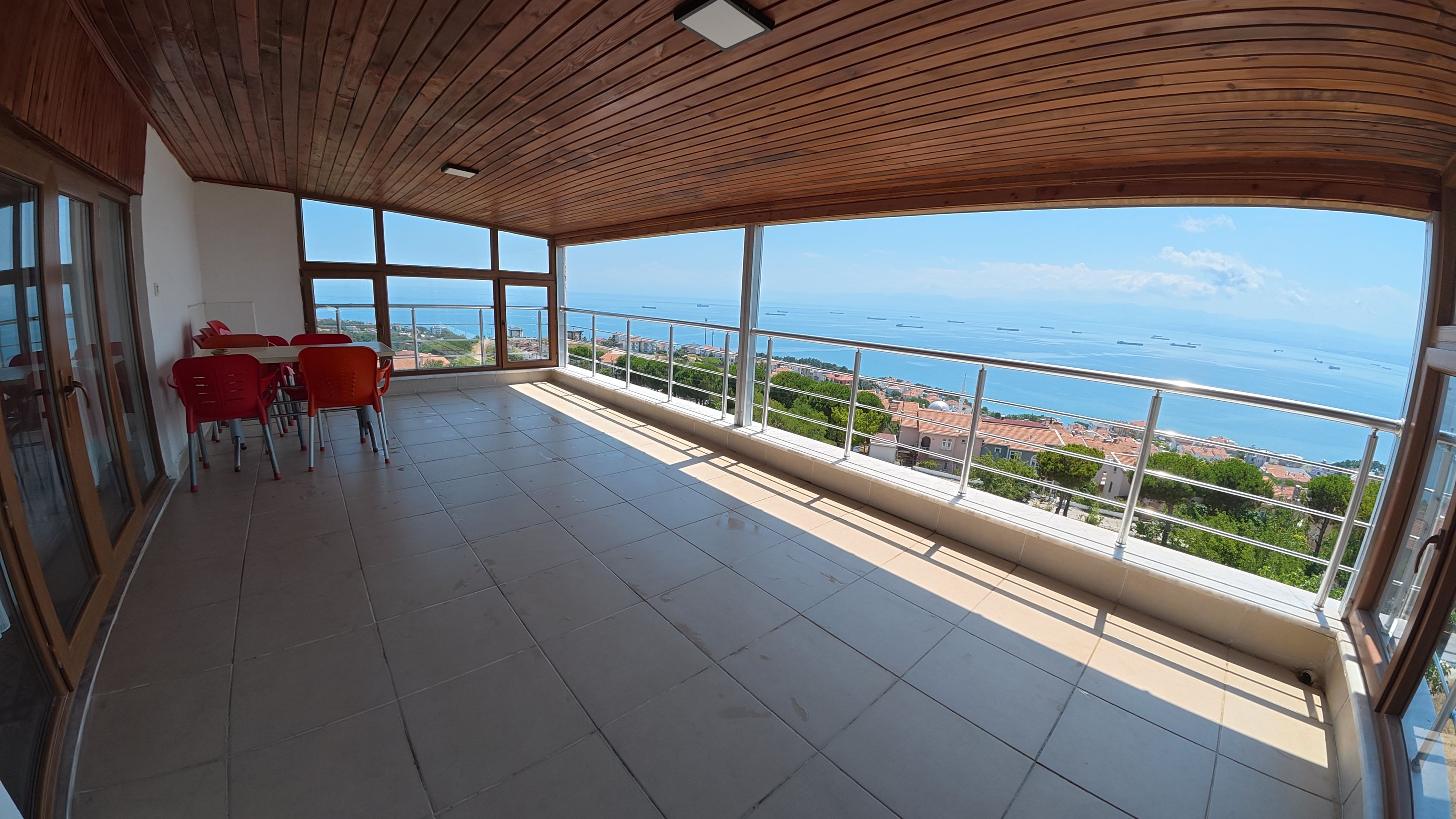 A balcony with a view of the sea, red chairs, and a tiled floor.