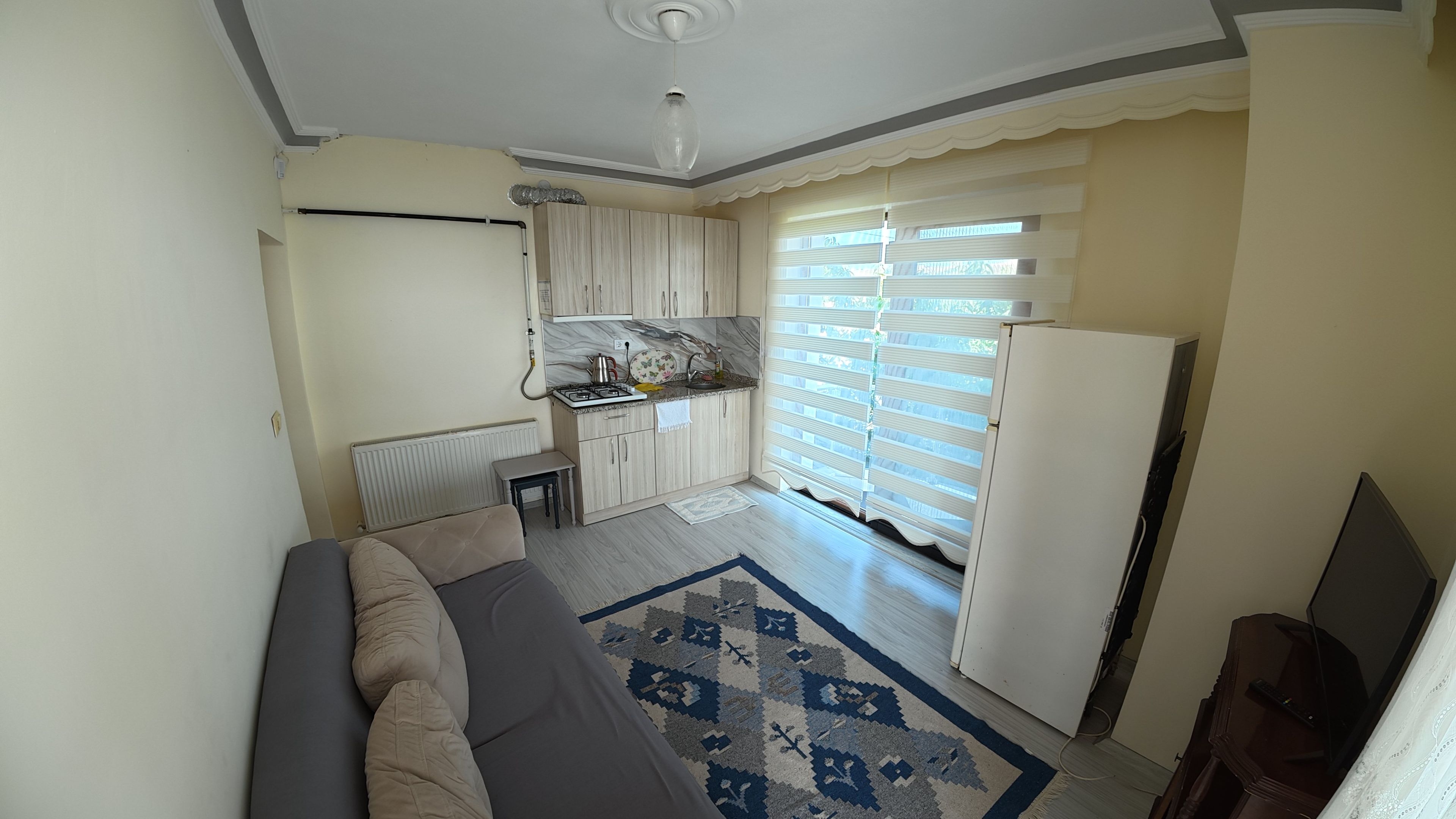 Un espacio habitable funcional con kitchenette, un sofá y un tapete estampado.