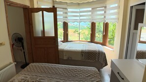A room with two beds, a fan, and a view of greenery through large windows. - Ozcan Apart Pansiyon (Sinop)