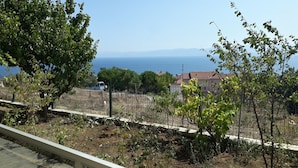 Un balcón con vista a la costa, incluyendo una baranda, árboles y una lejana vista del mar y edificios.