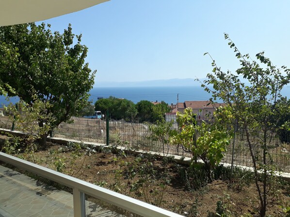 Un balcón con vista a la costa, incluyendo una baranda, árboles y una lejana vista del mar y edificios.