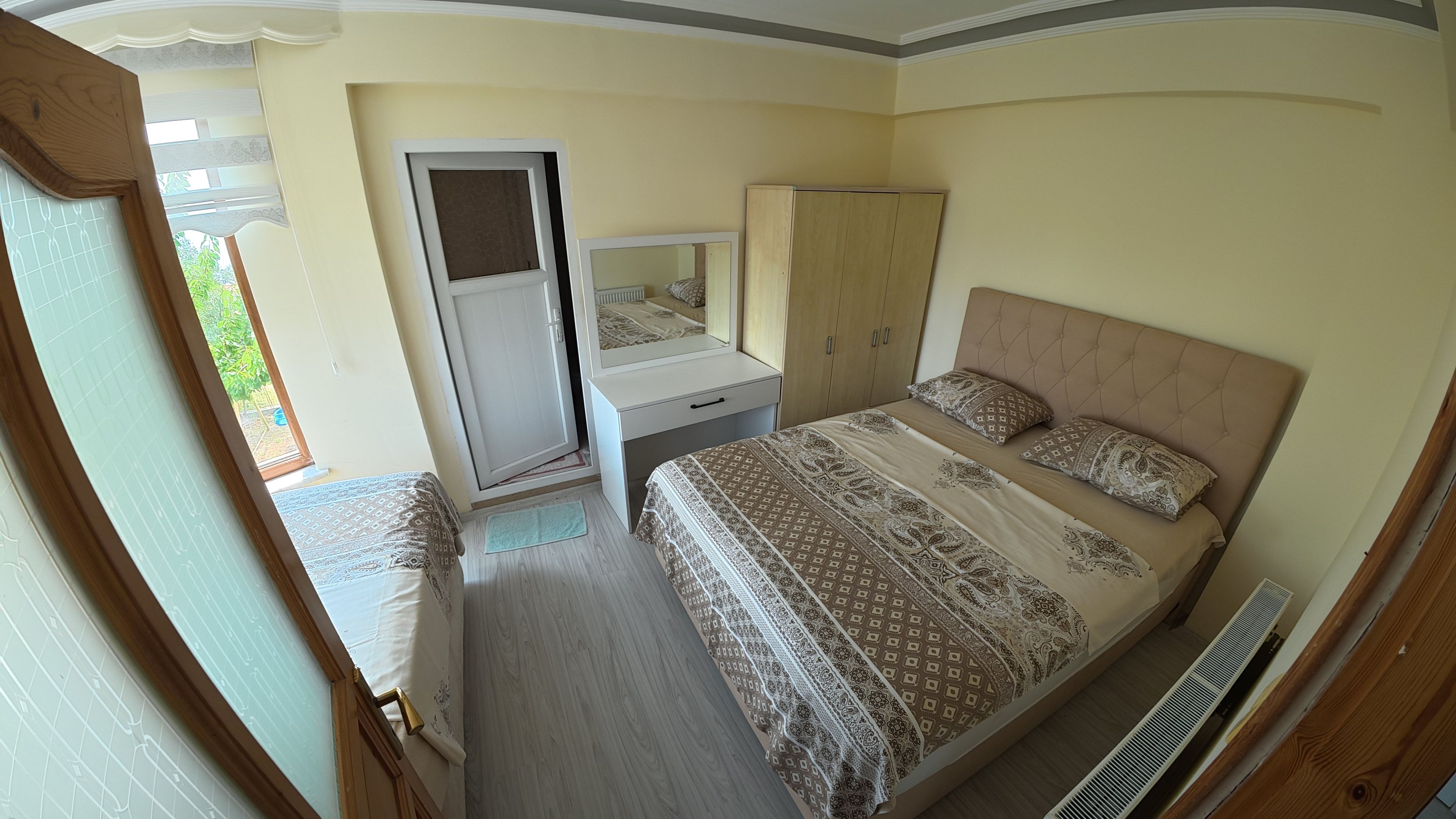 Un dormitorio con cama, armario, espejo y ventana.