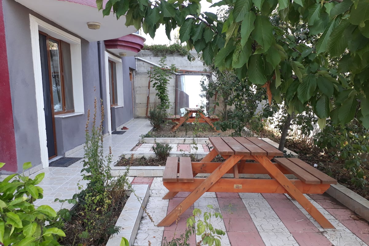 A courtyard with a wooden picnic table, surrounded by potted plants and a small garden area.