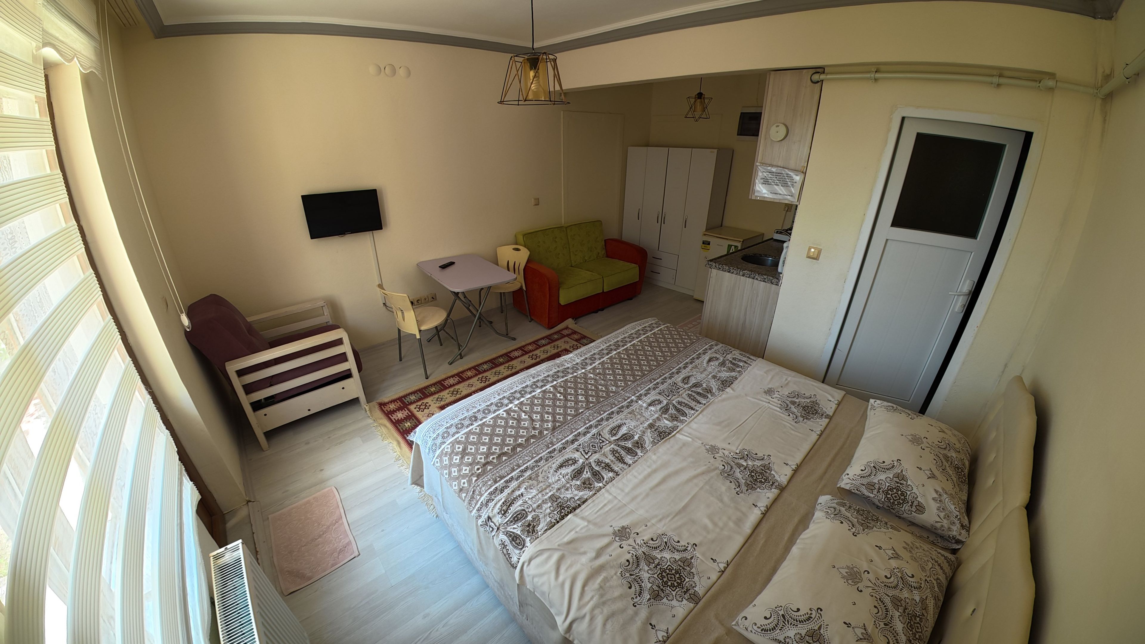 A bedroom with a bed, a desk, a chair, a wardrobe, and a small kitchenette.