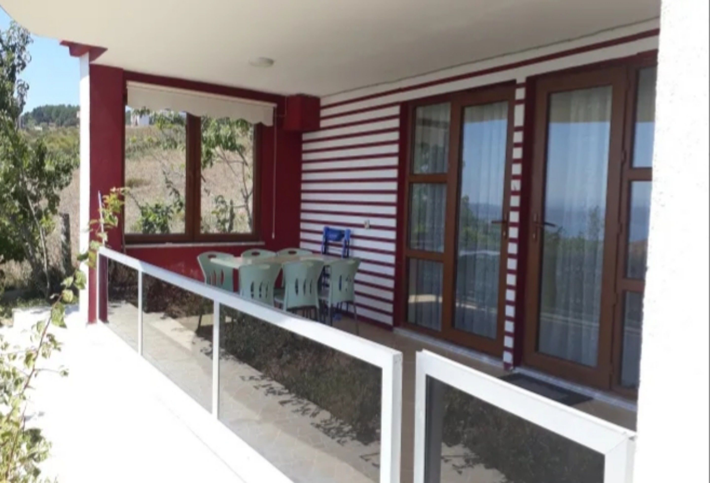 Un espacio al aire libre techado con barandilla blanca, una mesa con sillas y vistas al paisaje.
