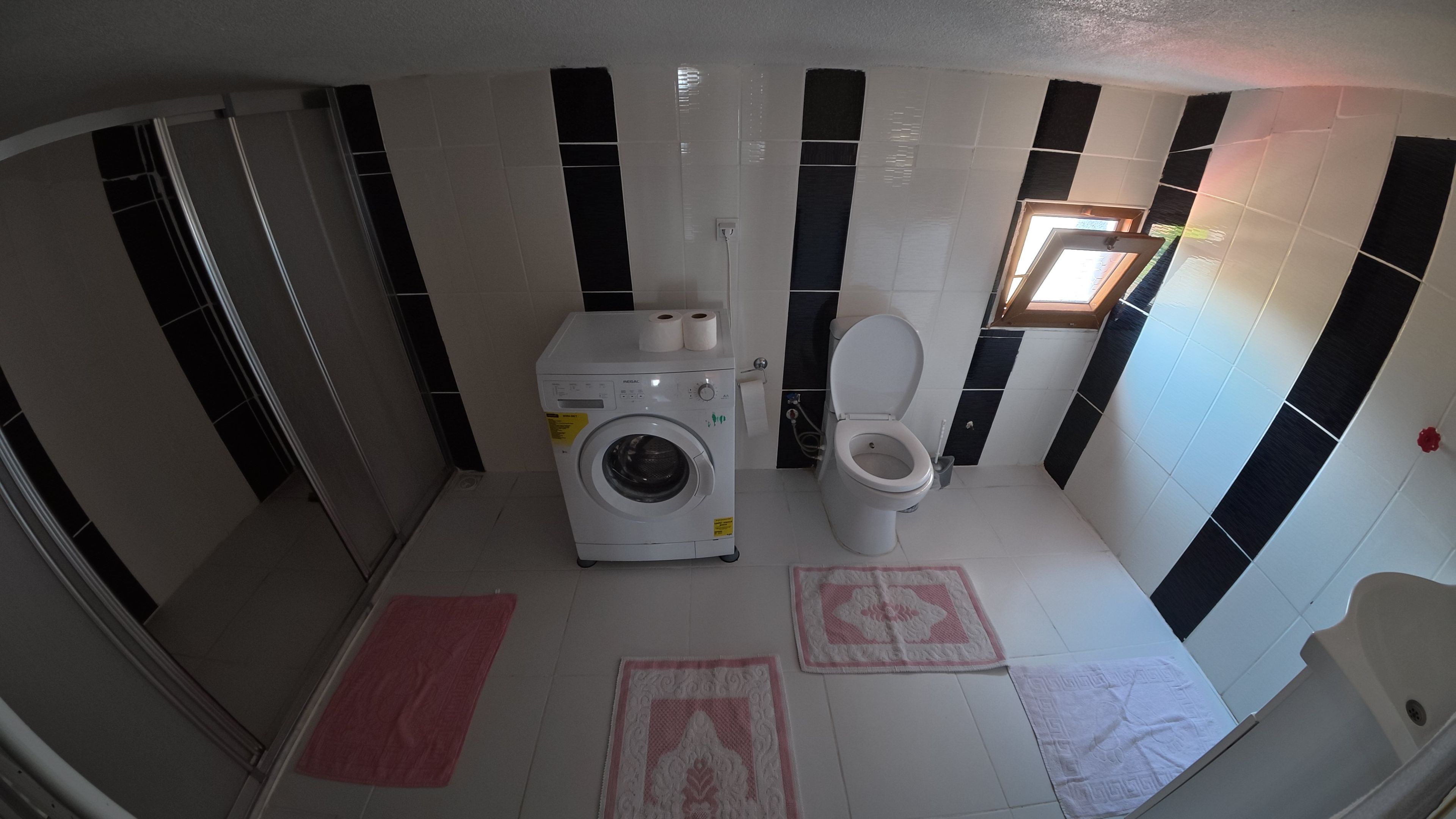 A compact bathroom with a washing machine, toilet, and a small window.