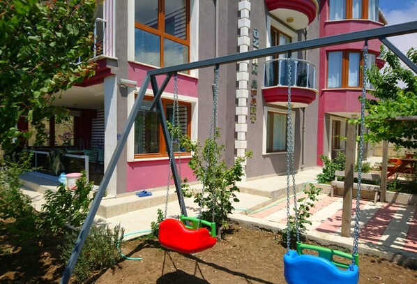 A playground with swings and a building in the background. - Ozcan Apart Pansiyon (Sinop)