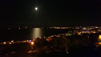 Vista nocturna de la costa con una luna brillante y luces distantes de la ciudad.