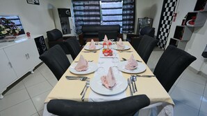 A dining area with a long table set for six, black chairs, and a white cabinet with a TV on the left. - Euro Japan Residence (Hassi Messaoud)