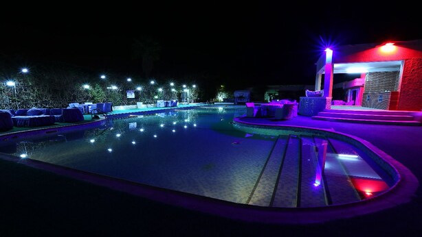 A nighttime swimming pool area with lounge chairs and a small building with a red-lit entrance. - Euro Japan Residence (Hassi Messaoud)