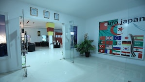 A modern lobby with a glass door entrance, a large poster of the Euro Japan Group, and a potted plant. - Euro Japan Residence (Hassi Messaoud)