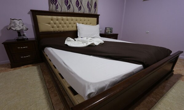 A neatly made bed with a headboard, a bedside table with a lamp, and a nightstand with a book.