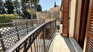 A balcony with a metal railing, a wooden door, and a view of trees and a building in the background. - S171 - Sirolo, wonderful studio in the center (Sirolo)