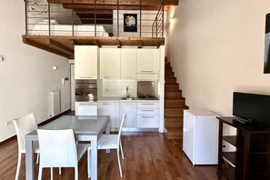 A modern kitchen with white cabinets, a dining table with chairs, a refrigerator, and a TV stand.
