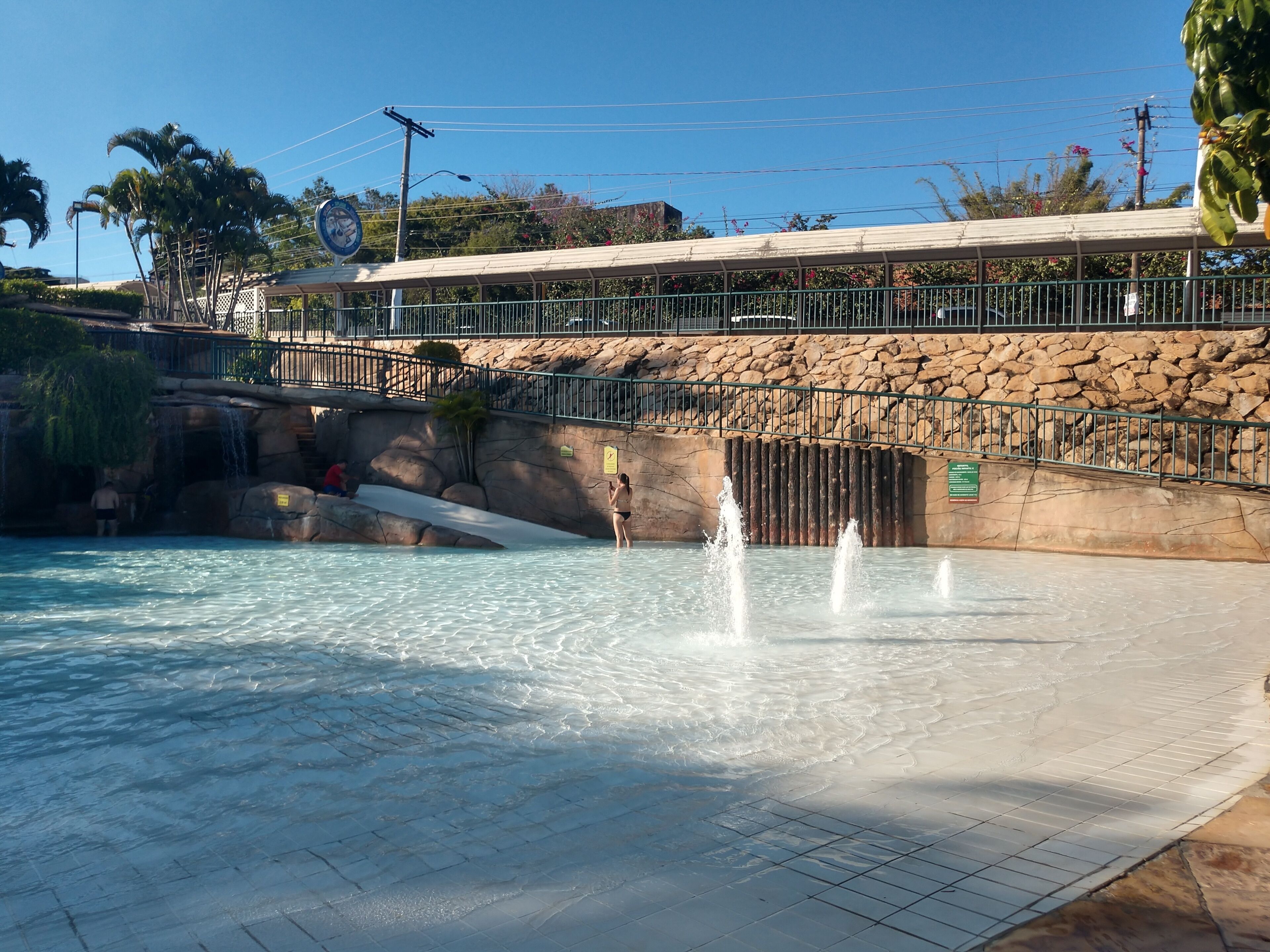 Ein Pool mit Wasserfall, einer Steinmauer und einem überdachten Gang.