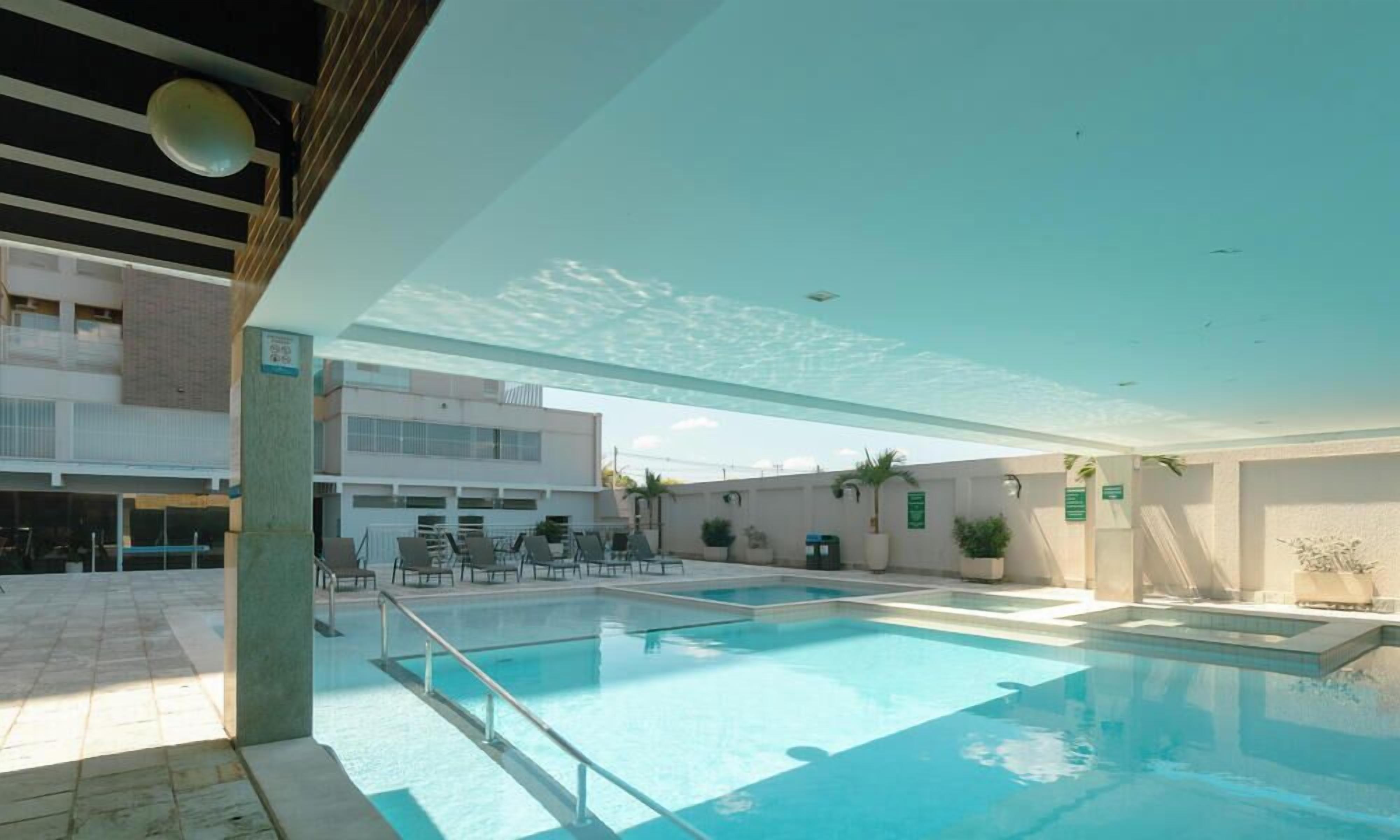 An indoor swimming pool with clear water, surrounded by lounge chairs and potted plants.