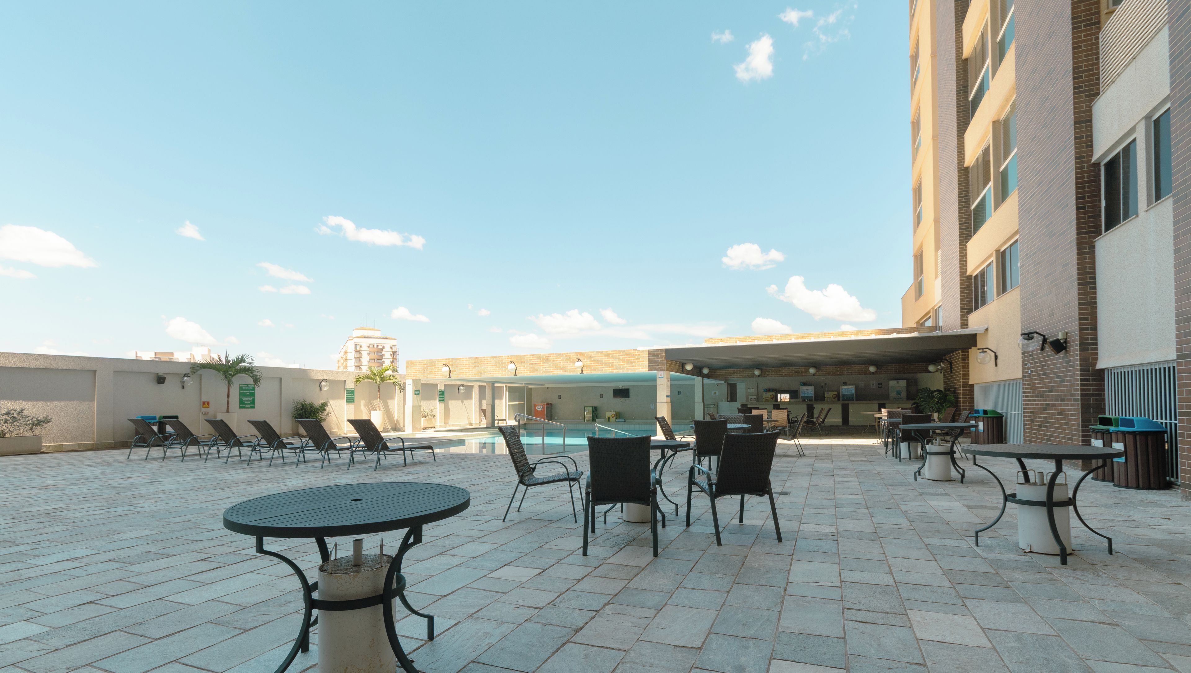 An outdoor patio area with tables and chairs, a pool, and a building in the background.