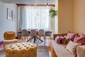A modern living room with a sofa, ottoman, dining table, chairs, and a hanging plant.