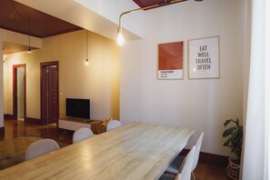 Uma sala de estar moderna com uma mesa de jantar de madeira, uma TV de tela plana e dois cartazes motivacionais emoldurados na parede.