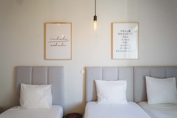 Two beds with grey headboards and white bedding, a light bulb hanging above, and two framed signs with text on the wall.
