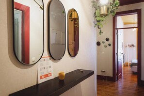 Un pasillo con un mostrador negro, tres espejos, una lámpara y una puerta que da a otra habitación.