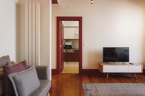 A living room with a sofa, a television on a stand, and a wooden floor.