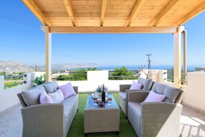 A covered outdoor seating area with wicker furniture and a table set for two, overlooking a scenic landscape. - Casa Vasilia Traditional Home (Chania)