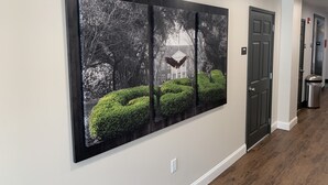 A hallway with a large black and white photograph of a tree-lined landscape and a building. - Stay Plus Extended Stay Suites (Statesboro)