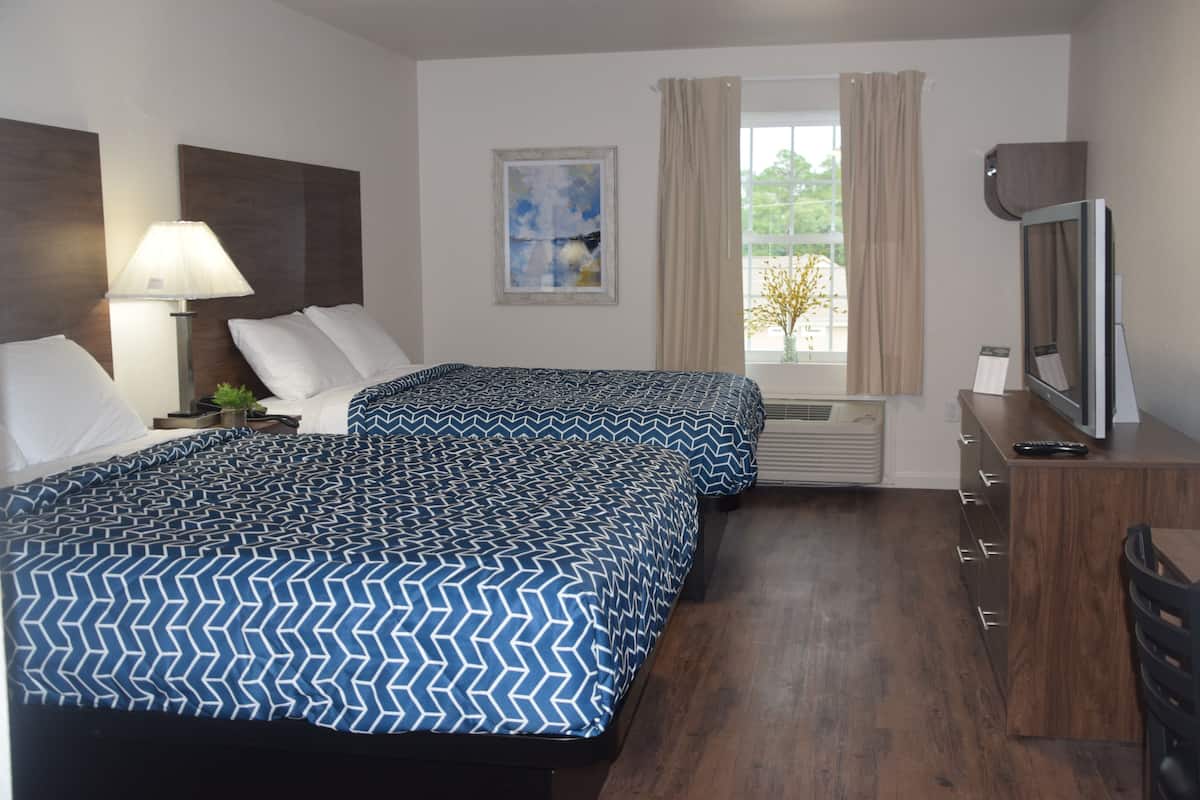 Une chambre d’hôtel avec deux lits, une télévision, un bureau et une fenêtre avec des rideaux.