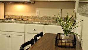 A kitchen with white cabinets, a granite countertop, a wooden dining table, and a potted plant. - Stay Plus Extended Stay Suites (Statesboro)