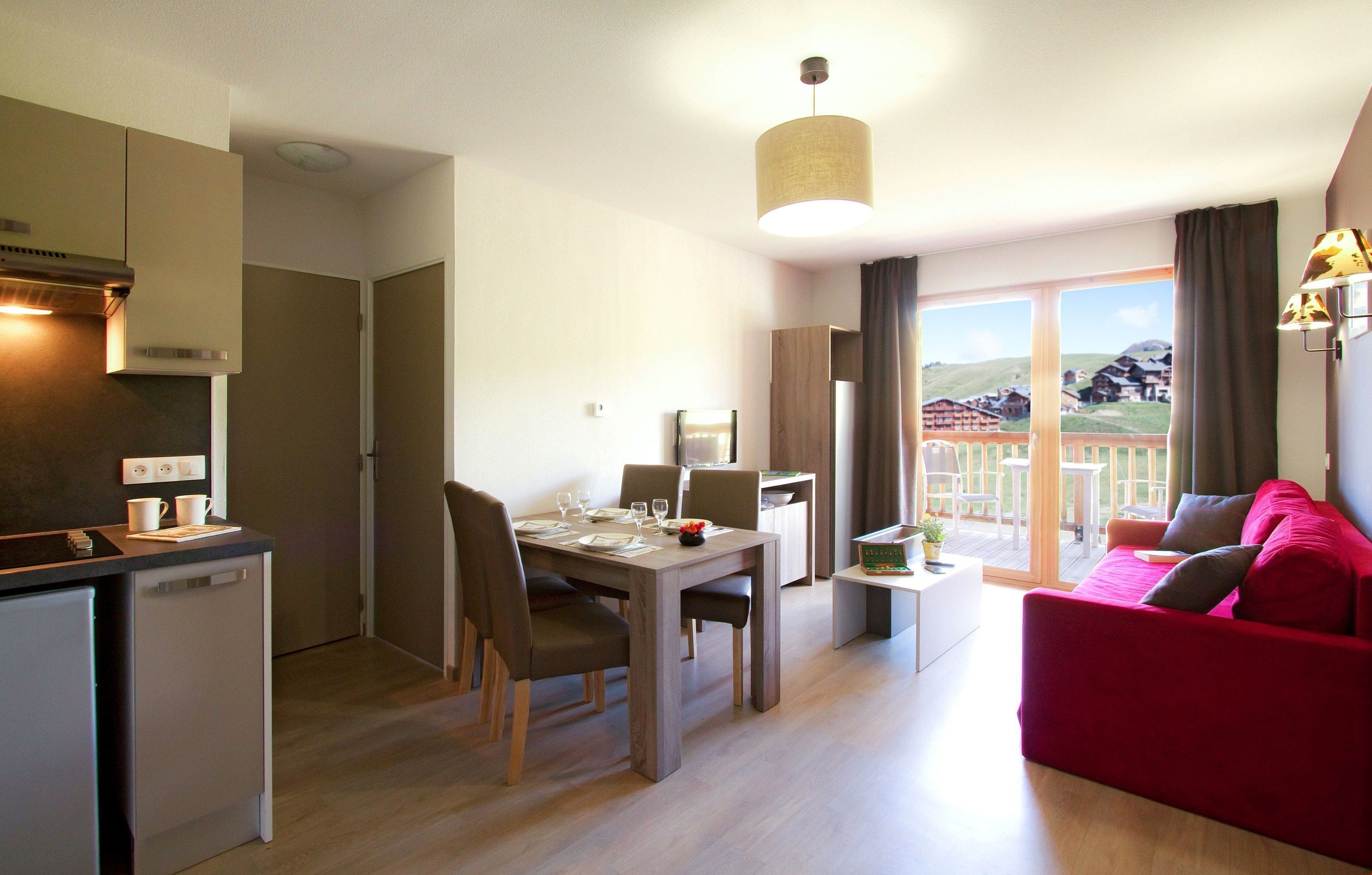 Une cuisine moderne avec un coin repas, un canapé rouge et un balcon offrant une vue sur les maisons.