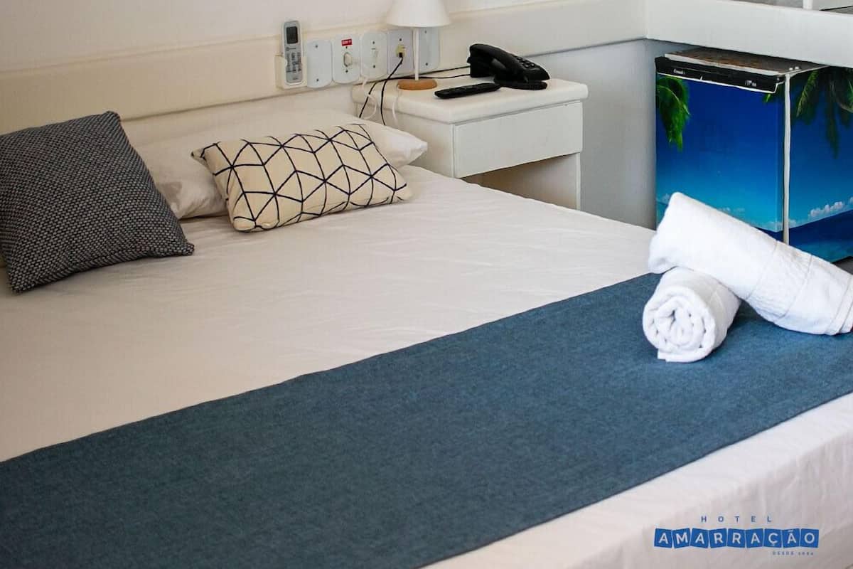 A hotel room with a bed, a nightstand, a lamp, a phone, and a towel.