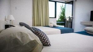 Habitación de hotel con dos camas, una lámpara, un televisor y una ventana con vistas a zonas verdes.