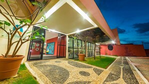 Un edificio moderno con fachada de vidrio, zona de entrada con baldosas y plantas en macetas.