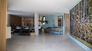 Un vestíbulo amplio con un cuadro grande, una zona de estar con sofá y sillones, y un mostrador de recepción de madera.