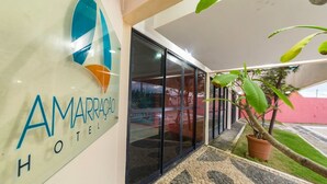 El exterior del Hotel Amarra, con una entrada de vidrio, un sendero adoquinado y una planta en maceta.