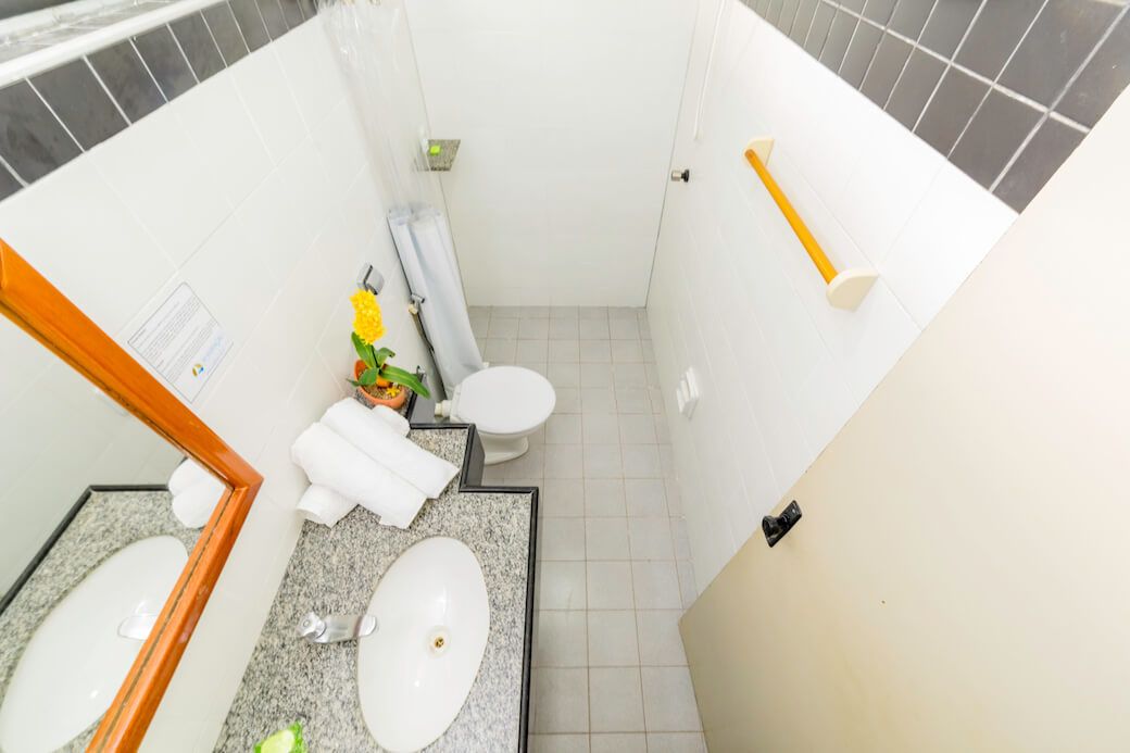 A compact bathroom with a white sink, two toilets, a shower, and a towel rack.
