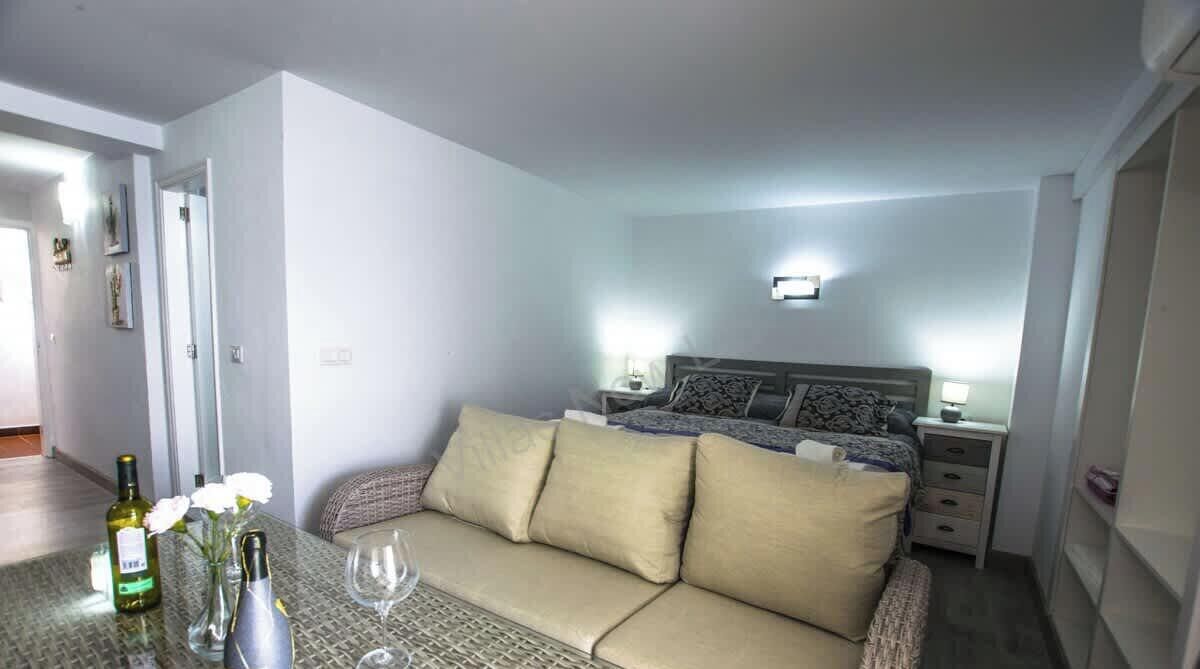 A bedroom with a bed, bedside tables, a sofa, and a glass table with bottles and glasses.