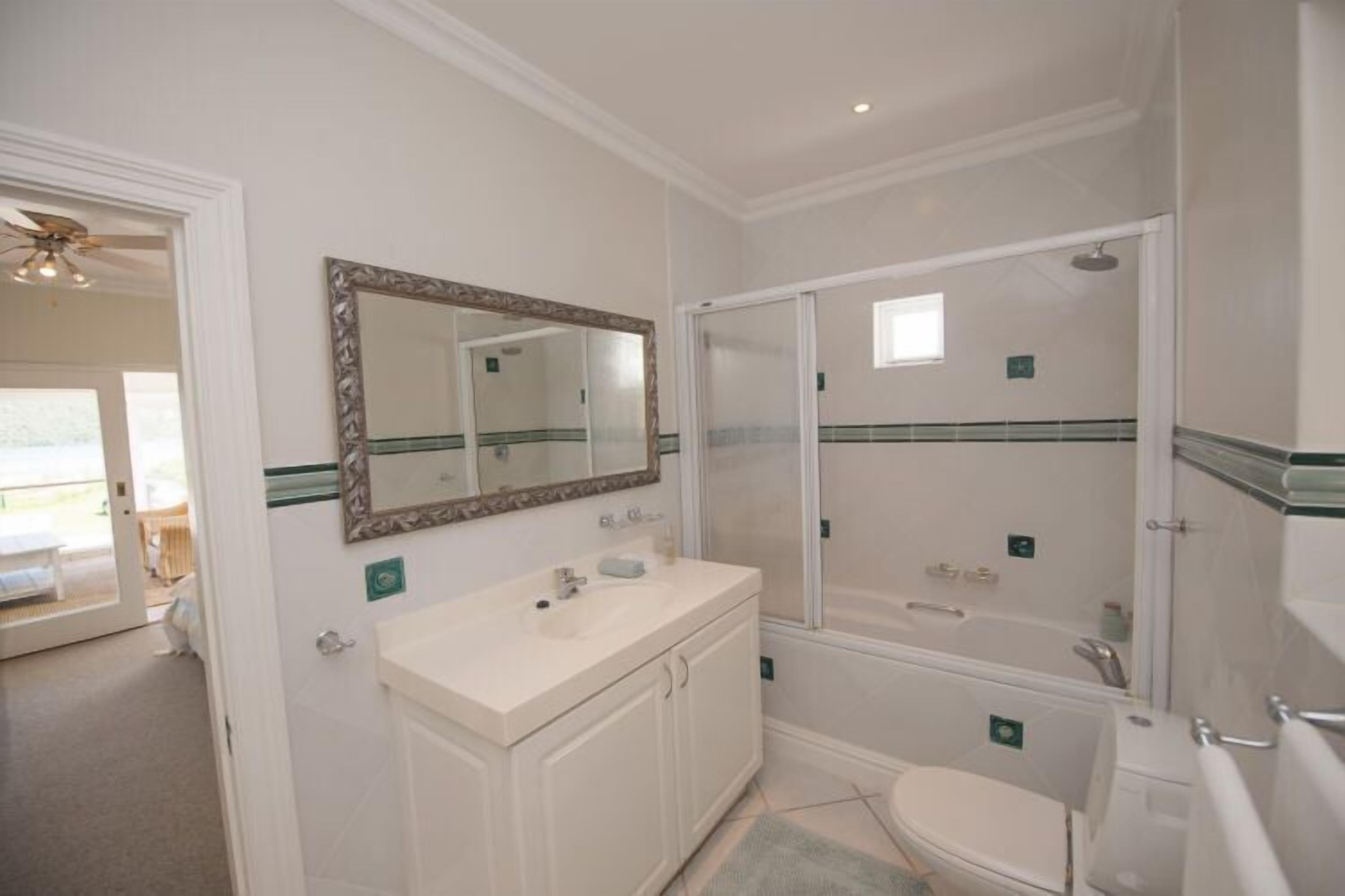 Une salle de bain avec un meuble-lavabo blanc, un grand miroir, une cabine de douche et des toilettes.