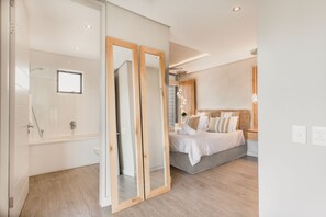 A modern bedroom with a large bed, a wooden wardrobe, and a bathroom with a bathtub and shower. - 16 Sloane Square (Cape Town)