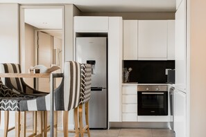 A modern kitchen with white cabinets, a stainless steel refrigerator, a Bosch oven, and a dining area with patterned chairs. - 16 Sloane Square (Cape Town)