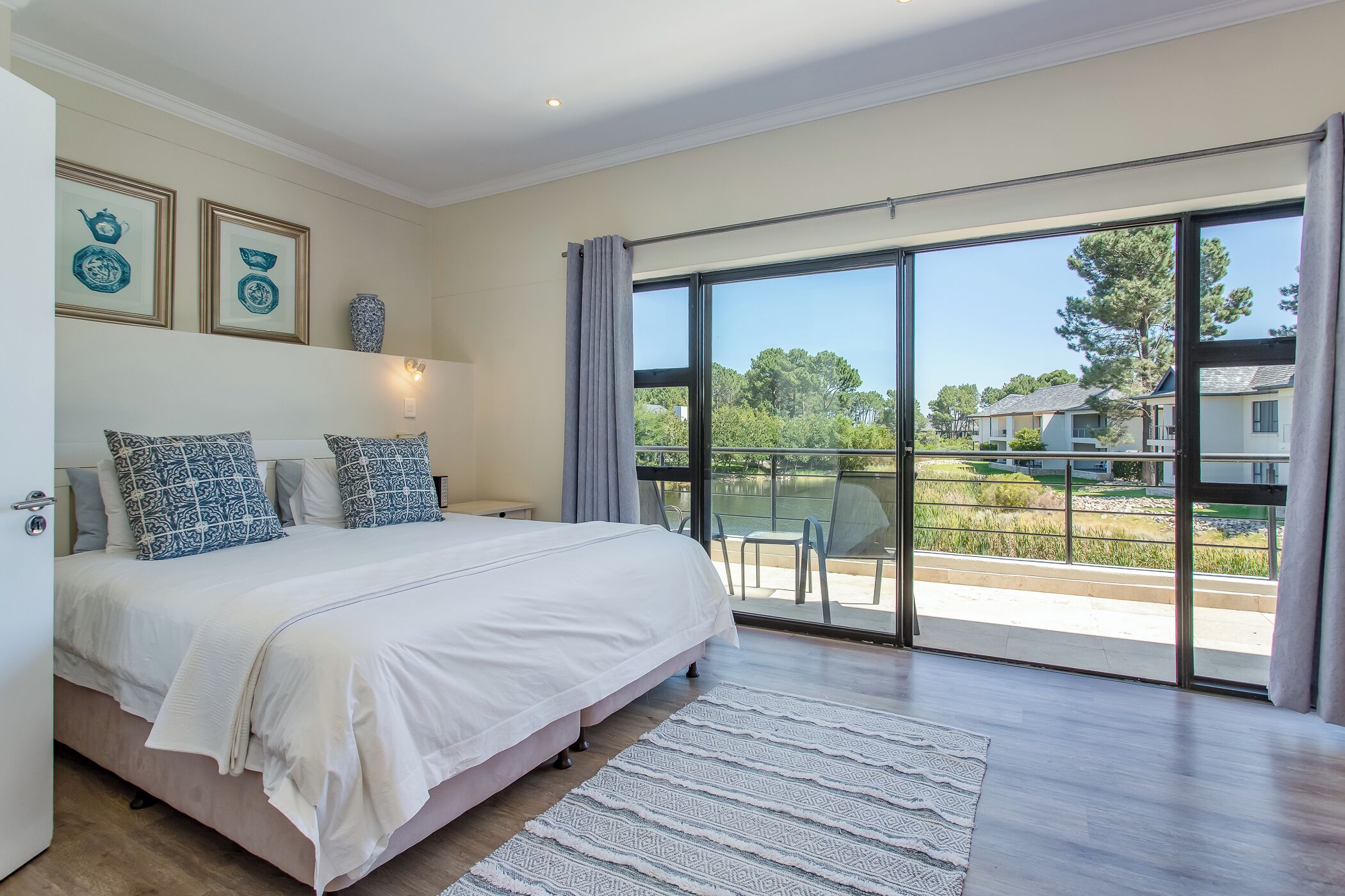 A bedroom with a large bed, a view of the outdoors through a sliding glass door, and framed artwork on the wall.
