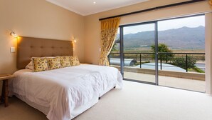 A bedroom with a large bed, a headboard, and a view of mountains through a sliding glass door. - Valley Golf Lodges (Paarl)