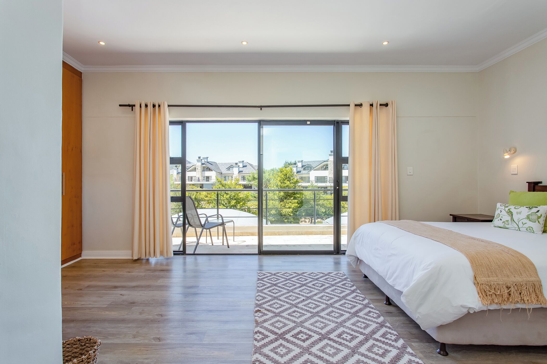 A bedroom with a large bed, a patterned rug, and a view of a balcony with a chair.