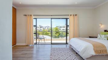 A bedroom with a large bed, a patterned rug, and a view of a balcony with a chair.